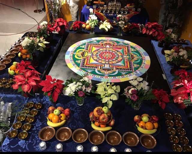 Sand mandala surrounded by offering bowls, fruit, and flowers